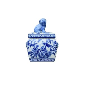 May include: A blue and white porcelain jar with a lid featuring a small blue and white dog figurine. The jar has a floral design and a geometric border.
