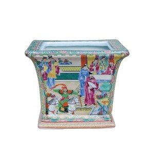 May include: A square porcelain planter with a colorful Chinese scene painted on the sides. The scene features people, horses, and buildings in a traditional style. The planter has a light green glaze and a white background.