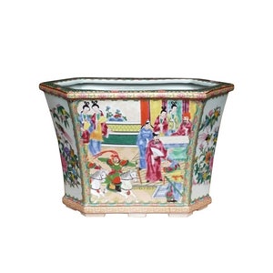 May include: A hexagonal porcelain planter with a white background and colorful floral and figural designs. The planter features a scene of people in traditional Chinese clothing, riding horses, and holding fans. The planter has a green, red, and gold trim.
