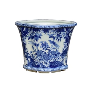 May include: A white ceramic planter with a blue and white floral design. The planter has a scalloped rim and a geometric pattern around the base.