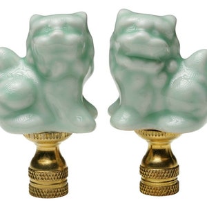 May include: A pair of green ceramic lamp finials shaped like foo dogs. The finials have gold bases.