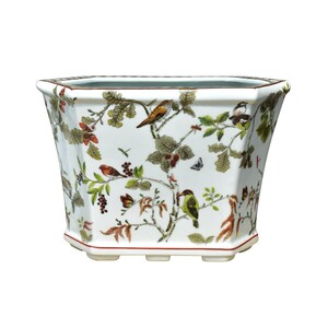 May include: White hexagonal ceramic planter with a floral and bird design. The planter has a red rim and a red line around the base.