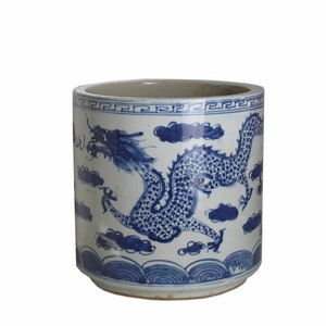 May include: A cylindrical ceramic container with a blue and white dragon design. The dragon is depicted with intricate scales and is surrounded by clouds. The container has a decorative border at the top and bottom, and is likely a decorative item.