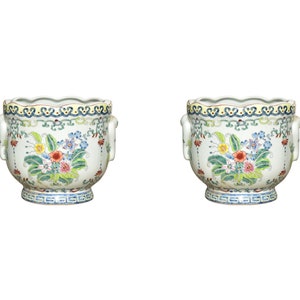 May include: Two white ceramic planters with floral designs and scalloped rims. The planters have two handles on each side and a blue and yellow border around the top.