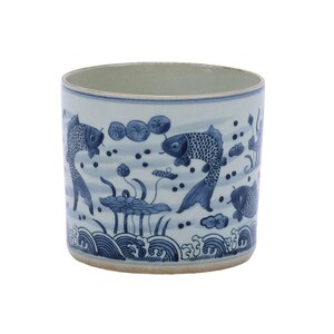 May include: A white ceramic cylinder with a blue and white design of fish swimming in water with lotus flowers. The cylinder has a smooth, glazed surface.