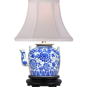 May include: A blue and white porcelain teapot lamp with a white lampshade. The teapot has a floral design and is on a black wooden base.