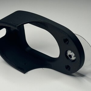 Puede incluir: Soporte para tel&eacute;fono de pl&aacute;stico negro con una ventosa en la parte posterior. El soporte tiene un dise&ntilde;o curvo para adaptarse a un tel&eacute;fono.