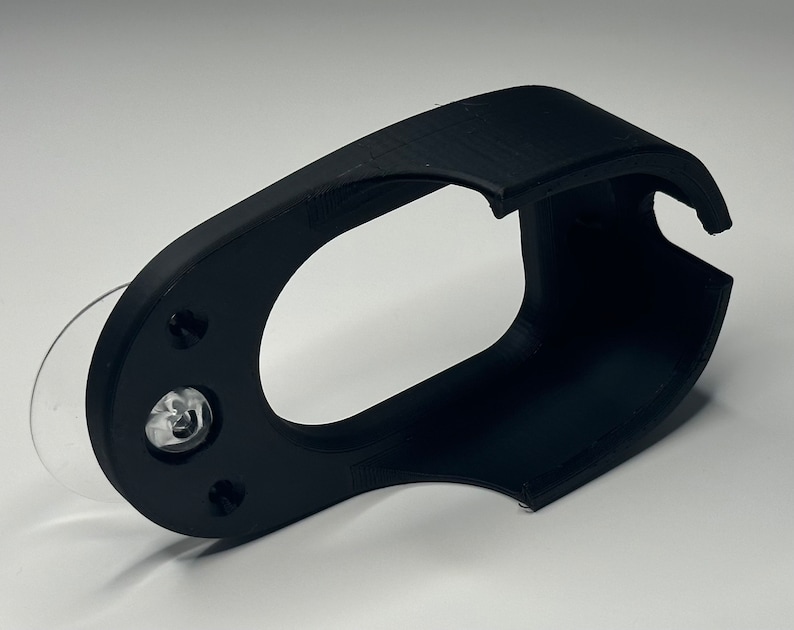 Puede incluir: Soporte para tel&eacute;fono de pl&aacute;stico negro con una ventosa en la parte posterior. El soporte tiene un dise&ntilde;o curvo y una gran abertura para un tel&eacute;fono.