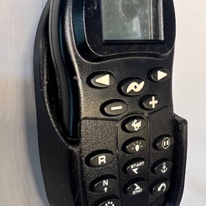 Puede incluir: Un mando a distancia i-Pilot negro con una pantalla y una variedad de botones. El mando a distancia est&aacute; montado en un soporte de pl&aacute;stico negro.