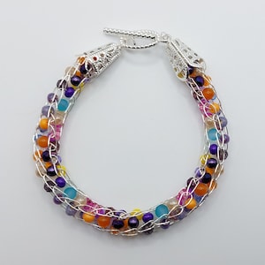 May include: A silver wire wrapped bracelet with colourful beads in shades of purple, orange, yellow, and blue.