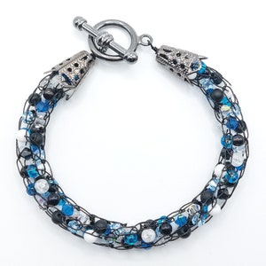 Può includere: Un braccialetto in filo nero con perline blu, bianche e nere. Il braccialetto ha una chiusura a scorrimento argentata.