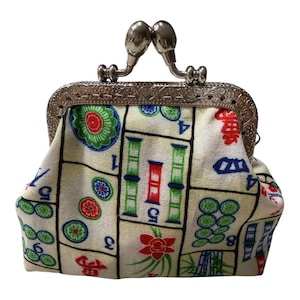 May include: A small, cream-colored coin purse with a silver clasp. The fabric is patterned with colorful Mahjong tiles in red, green, blue, and black. The purse has a kiss-lock closure.