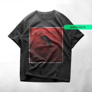 May include: Black t-shirt with a red and white graphic of a crow and the text "Escape the Fate" in a black font. The text "Unbreakable" is in a smaller font below the graphic.