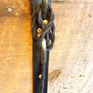 May include: Black electrical cord wrapped around a metal hook attached to a black metal plate. The plate is mounted to a wooden surface.