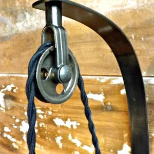 May include: Black metal wall mount with a pulley and black cord. The mount is curved and has a decorative design.