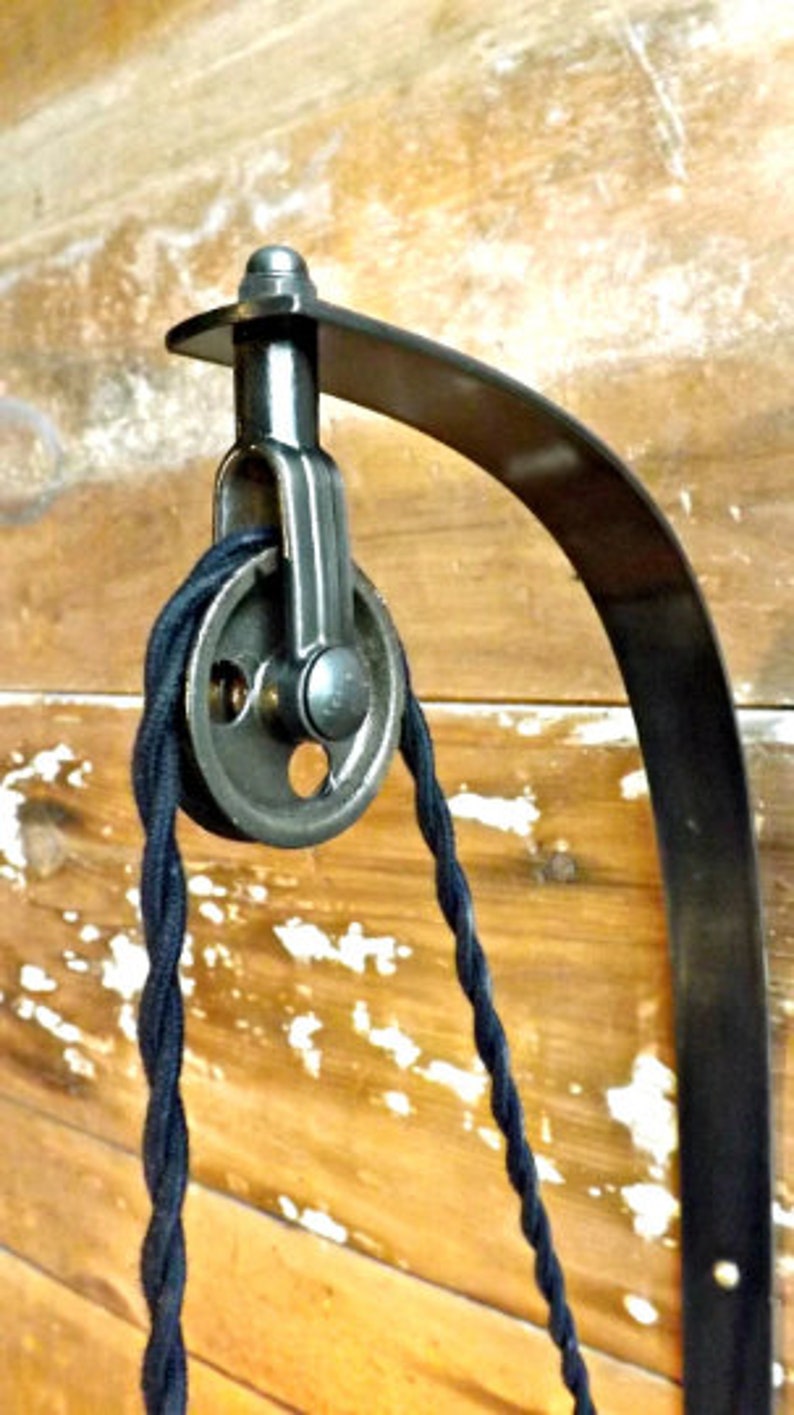 May include: Black metal wall mount with a pulley and black cord. The mount is curved and has a decorative design.