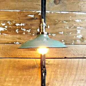 May include: A green metal lampshade with a black cord and a metal bracket attached to a wooden wall. The lampshade is hanging from the bracket and has a light bulb inside.