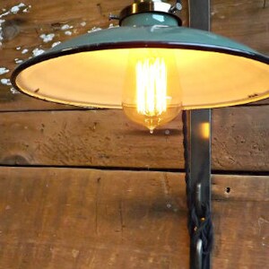 May include: A green metal ceiling light fixture with a white interior shade and a vintage-style light bulb. The light is mounted on a black metal bracket and is hanging from a black cord.