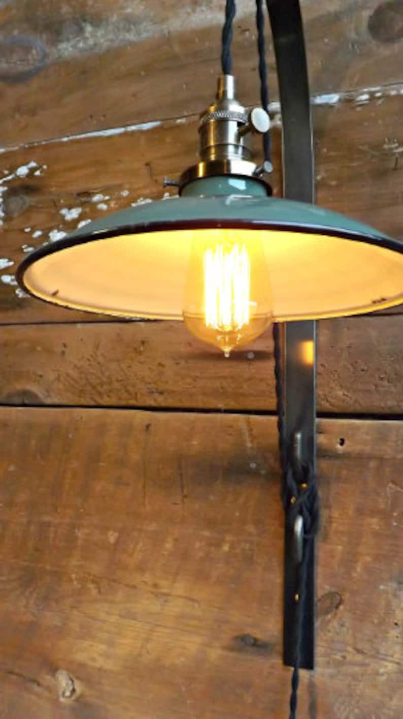 May include: A green metal ceiling light fixture with a white interior shade and a vintage-style light bulb. The light is mounted on a black metal bracket and is hanging from a black cord.