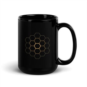 May include: Black ceramic mug with a gold honeycomb design. The honeycomb pattern is centered on the mug and features a gradient of gold hues. The mug has a large handle and a glossy finish.