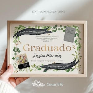 May include: A framed certificate with the word "Graduado" in gold lettering. The certificate includes text in Spanish, a watercolor floral border, and a small image. The frame is light brown.