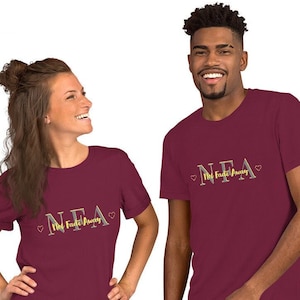 May include: Two people wearing maroon t-shirts with the text "NEA Not Fade Away" in gold and gray lettering with a heart on each side of the text.