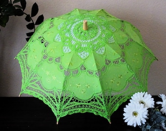 May include: A lime green lace parasol with a wooden handle. The parasol features intricate floral and geometric lace patterns. The parasol is open, showcasing the delicate design and craftsmanship. The parasol is a decorative item.