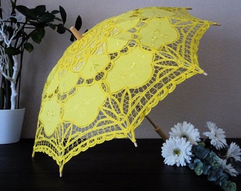 May include: A yellow lace parasol with a wooden handle. The parasol is closed and has a delicate floral pattern.
