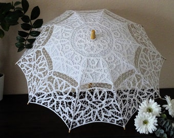 May include: A white lace parasol with a wooden handle. The parasol is open and the lace is intricate and delicate.