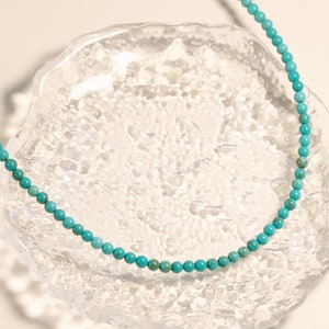 Puede incluir: Un collar de cuentas azul turquesa sobre una superficie de vidrio transparente.