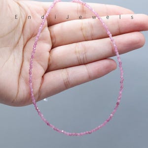 May include: A delicate pink gemstone necklace. The necklace is composed of small, round, pink gemstones strung together. The necklace is displayed on a light gray background. The word "Endi Jewels" is printed on the top left of the image.