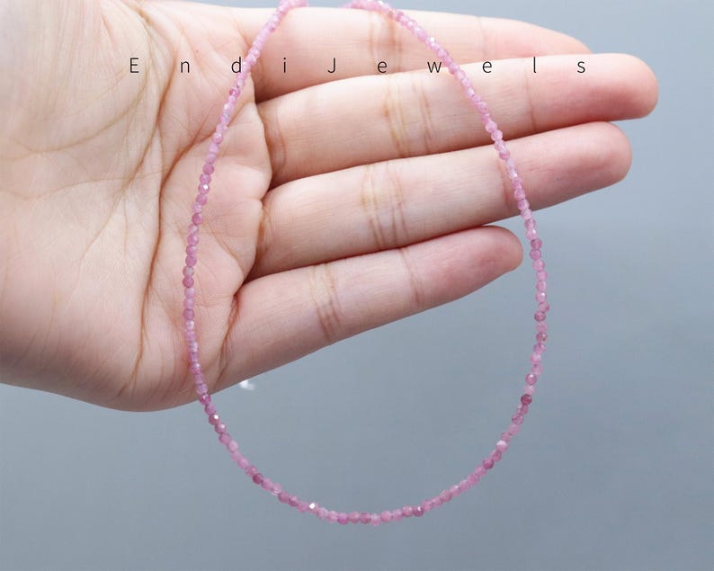 May include: A delicate pink gemstone necklace. The necklace is composed of small, round, pink gemstones strung together. The necklace is displayed on a light gray background. The word "Endi Jewels" is printed on the top left of the image.