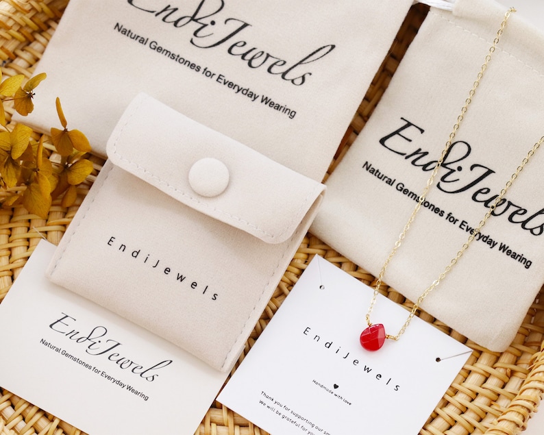 May include: A red gemstone necklace with a gold chain and a small red heart pendant. The necklace is displayed on a white velvet pouch with the text "Endi Jewels" and "Natural Gemstones for Everyday Wearing".