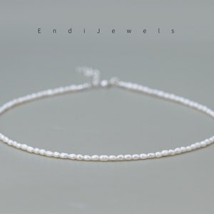 Puede incluir: Delicado collar de perlas blancas. El collar está compuesto por pequeñas perlas ovaladas ensartadas. El cierre es plateado. La marca "Endi Jewels" está impresa en la parte superior de la imagen.