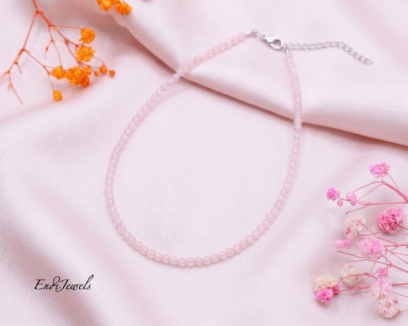 May include: A delicate necklace featuring small, round, pale pink beads strung together. The necklace includes a silver-toned metal lobster clasp and an adjustable extender chain. The text EndiJewels is visible in the bottom left corner.