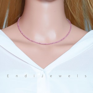 May include: A delicate pink beaded necklace. The necklace is a choker style, resting closely on the neck. The beads are small and evenly spaced, creating a subtle sparkle. The image also displays the text "Endi Jewels".