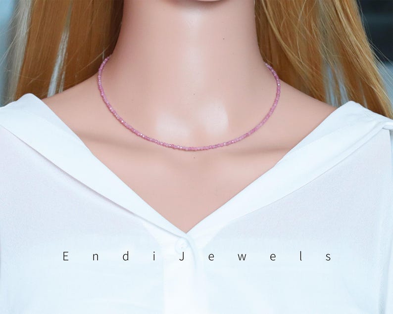 May include: A delicate pink beaded necklace. The necklace is a choker style, resting closely on the neck. The beads are small and evenly spaced, creating a subtle sparkle. The image also displays the text "Endi Jewels".