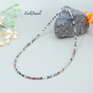 May include: A multi-colored gemstone necklace with a silver clasp. The necklace is made of small, round beads in shades of pink, green, black, and white.