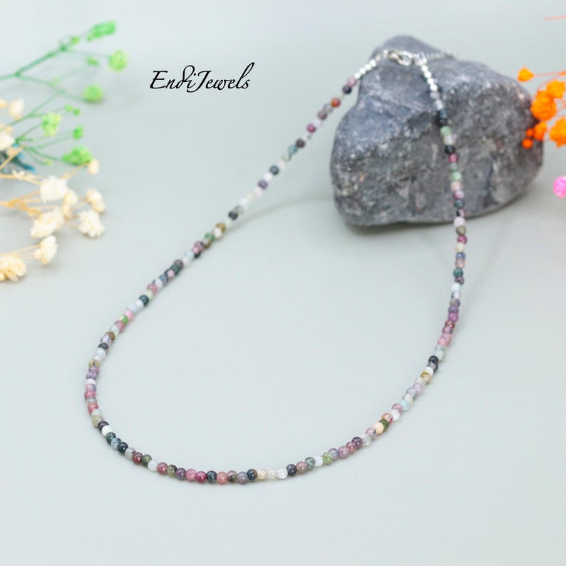 May include: A multi-colored gemstone necklace with a silver clasp. The necklace is made of small, round beads in shades of pink, green, black, and white.
