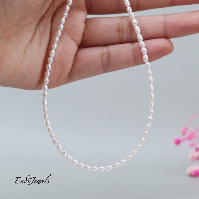 May include: A delicate white pearl necklace with a simple design. The necklace is made of small, round pearls that are strung together on a silver chain.