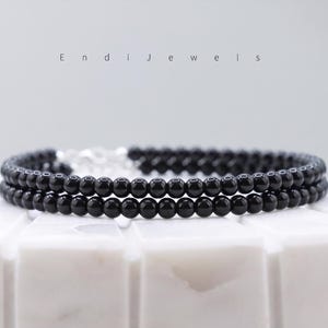 Puede incluir: Una pulsera de dos hilos con peque&ntilde;as cuentas negras brillantes. La pulsera est&aacute; conectada con un cierre plateado. El nombre de la marca "Endi Jewels" se muestra en una fuente minimalista encima de la pulsera.