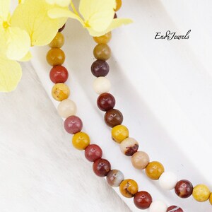 May include: A close-up of a multi-colored beaded necklace with red, brown, yellow, and white beads. The necklace is on a white surface. Endi Jewels is written in the top right corner of the image.