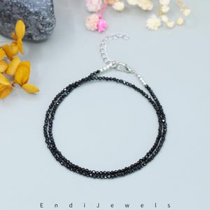 May include: A delicate black gemstone anklet with a silver clasp. The anklet is made of small, round black beads and is perfect for layering with other jewelry.