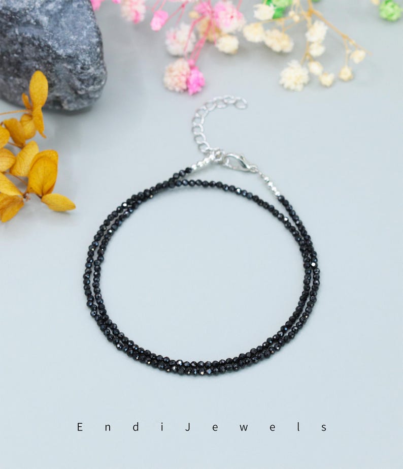 May include: A delicate black gemstone anklet with a silver clasp. The anklet is made of small, round black beads and is perfect for layering with other jewelry.