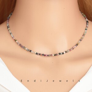 May include: A delicate necklace made of small, multi-colored beads. The beads are a mix of pink, green, and black, and they are strung on a silver chain.