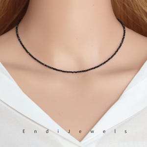 May include: A delicate black choker necklace made of small black beads. The necklace is worn by a model with a white shirt.