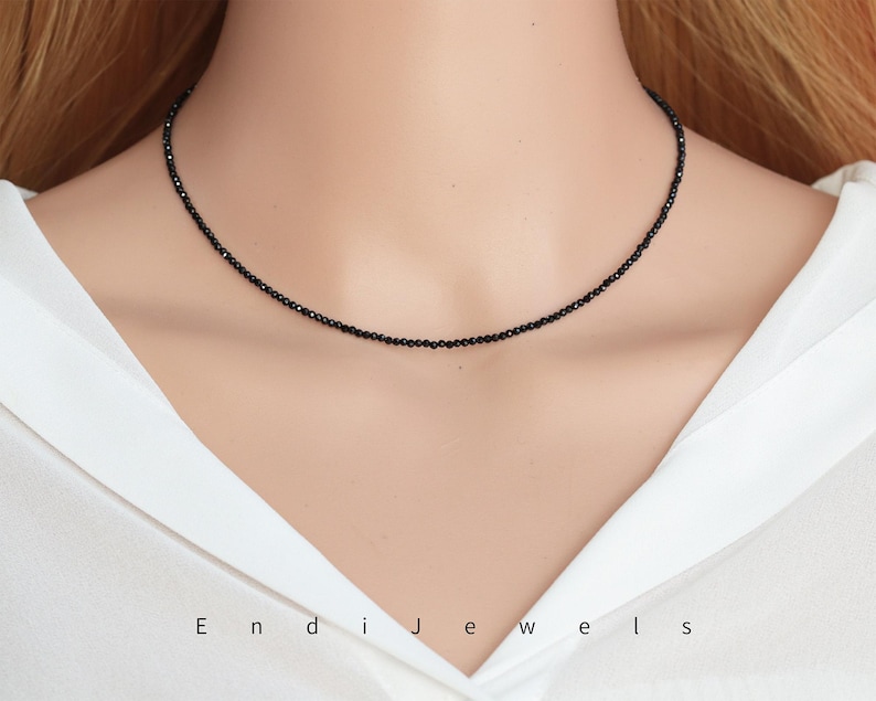 May include: A delicate black choker necklace made of small black beads. The necklace is worn by a model with a white shirt.