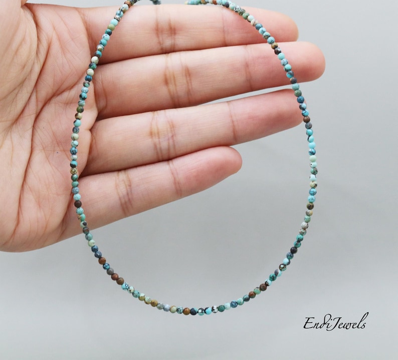 Op de afbeelding: Een delicate turquoise en bruine edelsteen ketting met kleine, ronde kralen. De ketting ligt op een hand, waardoor de lengte en grootte van de kralen zichtbaar zijn.