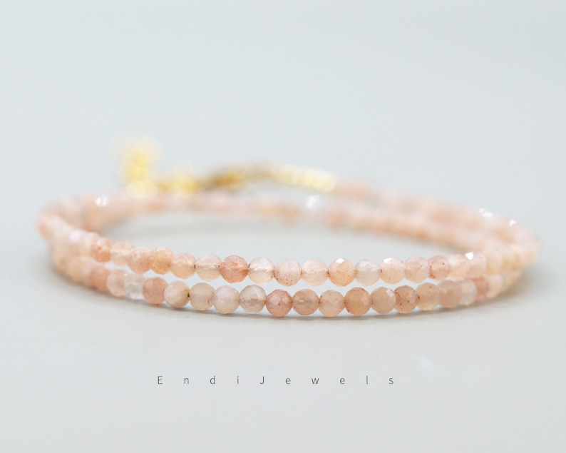K&ouml;nnte beinhalten: Ein zartes Armband mit zwei Reihen aus kleinen, hellrosa Sunstone-Perlen. Das Armband hat einen goldenen Verschluss.