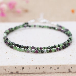May include: A delicate double-strand bracelet featuring green and pink gemstone beads. The bracelet is made with small, round beads and has a simple, elegant design.
